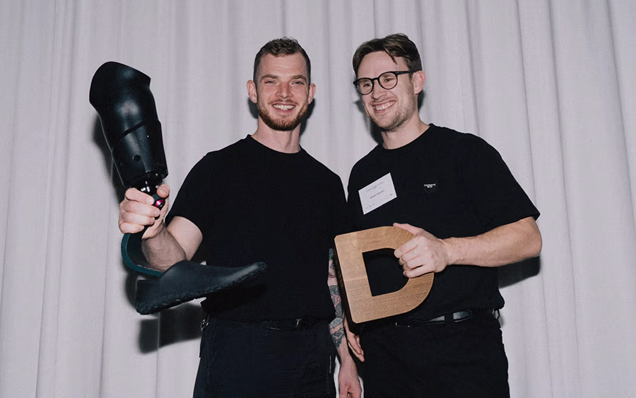 Trofeo Danish Design Award in quercia sorretto con due mani davanti a una tenda bianca